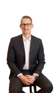 A man in a suit and glasses sitting down.